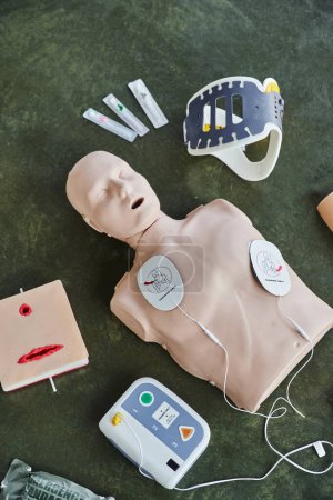 top view of CPR manikin, automated external defibrillator, wound care simulator, neck brace and syringes, medical equipment for first aid training and skills development