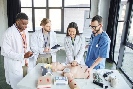 first aid training, cheerful asian woman practicing chest compressions on CPR manikin near medical instructor and multiethnic students writing in notebooks, emergency situations response concept