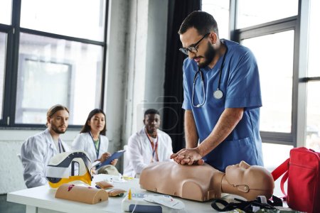 junge multikulturelle Studenten in weißen Mänteln schauen dem medizinischen Ausbilder zu, der bei einem Erste-Hilfe-Seminar Brustkompressionen an einer CPR-Schaufensterpuppe macht und dabei lebensrettende Fähigkeiten erwirbt und praktiziert