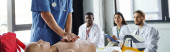 professional paramedic doing chest compressions on CPR manikin near multiethnic students in white coats during first aid seminar, acquiring and practicing life-saving skills concept, banner Poster #661888300