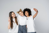 Smiling multiethnic teen friends in white t-shirts taking selfie on smartphone, hugging and gesturing while standing isolated on grey, teenagers bonding over common interest, friendship  Stickers #662018438
