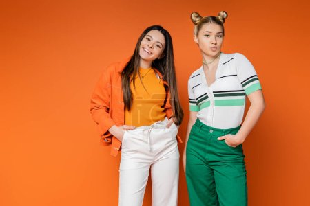 Photo for Confident and cheerful teenage girlfriends in casual outfits posing and pouting lips while looking at camera on orange background, fashionable girls with sense of style, friendship and bonding - Royalty Free Image