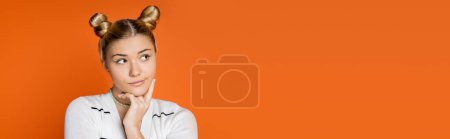 Porträt eines nachdenklichen Teenagers mit Frisur und buntem Make-up, der wegschaut, während er in lässiger Kleidung isoliert auf orangefarbenem, trendigem Teenie-Mädchen posiert, das Individualität ausdrückt, Banner mit Kopierraum 