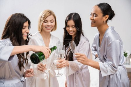 bridal shower, woman pouring champagne into glasses near interracial girlfriends, celebration, bride and bridesmaids, brunette and blonde, diversity, bridal shower, best friends, four women, festive