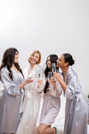 ducha nupcial, novias multiculturales sosteniendo copas con champán, celebración antes de la boda, morena y rubia, novia y sus damas de honor, diversas etnias, mujeres asiáticas y negras