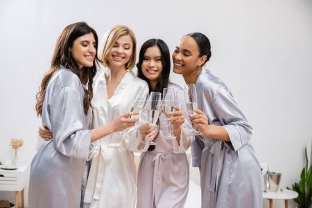 Brautparty, interrassische Freundinnen, die Gläser mit Champagner halten, Feier vor der Hochzeit, brünette und blonde Frauen, Braut und ihre Brautjungfern, verschiedene Ethnien, Positivität  