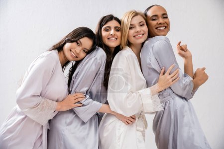 ducha nupcial, cuatro mujeres, novia feliz y damas de honor en túnicas de seda, mirando a la cámara, diversidad cultural, divertirse juntos, objetivos de amistad, morena y mujeres rubias 