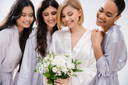 douche nuptiale, quatre femmes, mariée heureuse tenant un bouquet près des demoiselles d'honneur en robes de soie, diversité culturelle, s'amuser ensemble, objectifs d'amitié, femmes brunes et blondes, sourire et joie 