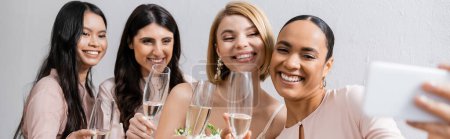 four women, beautiful bride and her interracial bridesmaids taking selfie together, happiness, champagne glasses, bridal bouquet, wedding dress, bridesmaid gown, brunette and blonde women, banner 