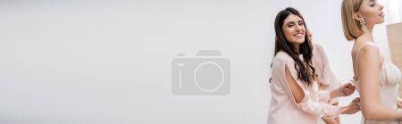 Foto de Servicio de dama de honor, mujer feliz cremallera vestido de novia blanco de novia rubia joven sobre fondo gris, moda, elegancia, ocasión especial, felicidad, preparativos de boda, bandera - Imagen libre de derechos