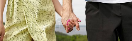 Ausgeschnittene Ansicht eines stilvollen Paares in Sommerkleidung, das Händchen hält, während es mit verschwommener Landschaft im Hintergrund steht, ländliches Fernweh und Liebeskonzept, Banner, Ruhe