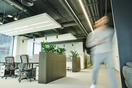Bewegungsunschärfe eines erfolgreichen, energiegeladenen Geschäftsmannes, der an einem Großraumbüro mit High-Tech-Interieur, modernen Möbeln und grünen natürlichen Pflanzen entlanggeht, zeitgemäßes Coworking-Umfeld