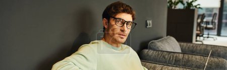 portrait of stylish businessman in casual clothes and eyeglasses looking at camera in contemporary office environment, professional headshot, confidence and success concept, banner