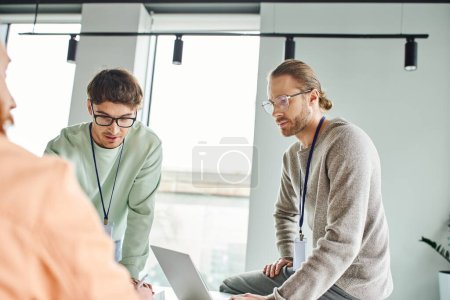 Photo for Serious and concentrated architects in eyeglasses and casual clothes working near laptop and business partner on blurred foreground in coworking space of modern design studio - Royalty Free Image
