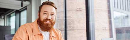 professional headshot of happy, charismatic and bearded businessman smiling at camera in contemporary office environment, portrait, business success concept, banner with copy space