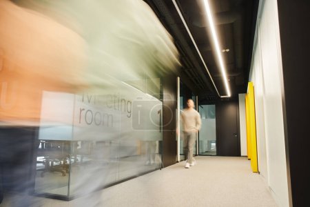 long exposure of energetic businessman walking along blurred meeting room in corridor of coworking environment in contemporary office, dynamic business concept