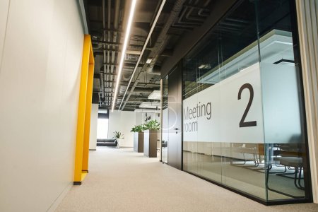 long and wide corridor with led lighting, green plants, meeting room behind glass transparent wall in modern coworking environment with high tech interior, workspace organization concept