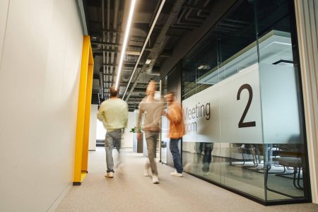 motion blur of energetic and ambitious businessmen walking in corridor of modern coworking environment with high tech interior along meeting room, dynamic business concept