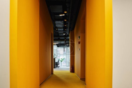 langer Flur mit Wänden in leuchtendem Orange in zeitgenössischem Coworking-Büro mit modernem High-Tech-Interieur, Arbeitsbereichskonzept