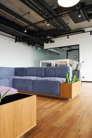 sofá suave y cómodo cerca de la mesa alta y sillas en el amplio salón de la oficina contemporánea, ambiente de coworking, interior de estilo de alta tecnología, concepto de organización del espacio de trabajo