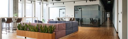 modern and spacious lounge with comfortable couch, high chairs near large windows, natural decor with green plants, coworking environment, workspace organization concept, banner