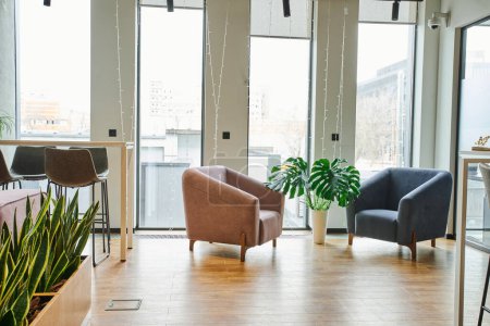 przestronny salon biurowy z dużymi oknami, przytulne i wygodne fotele, zielone i naturalne rośliny w nowoczesnym środowisku współpracowników, koncepcja organizacji miejsca pracy