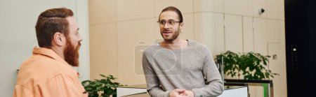 inspired entrepreneur in casual clothes and eyeglasses listening to bearded business partner talking about startup project in lobby of modern office environment, creative thinking, banner