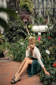 Trendy young african american woman in summer knitted top and skirt looking at camera while relaxing near flowers and plants in garden center, fashion-forward lady in midst of tropical greenery puzzle #663910544