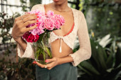 Cropped view of blurred african american woman in summer clothes holding vase with pink roses and standing in blurred garden center at background, trendy woman with tropical flair magic mug #663911496