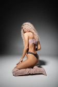 full length of passionate and stylish woman with wavy ash blonde hair and sexy buttocks, wearing lace underwear and long boots, sitting in provocative pose on black and grey background puzzle #663913460