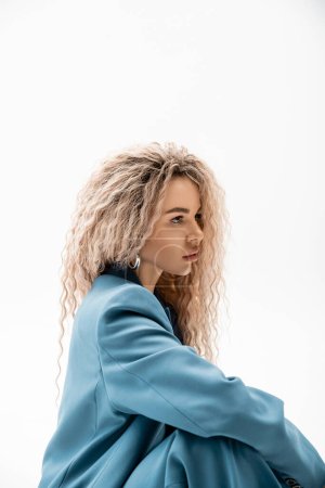Photo for Profile portrait of mesmerizing woman with wavy ash blonde hair wearing blue stylish blazer and looking away on grey background, charming and sensual female model, modern fashion - Royalty Free Image