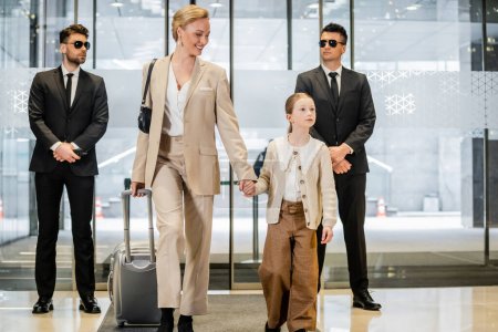 personal security service, two bodyguards in formal wear and sunglasses standing near hotel entrance, happy mother and child holding hands and walking with luggage, entering lobby, luxury lifestyle 