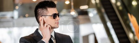Bodyguard-Konzept, gutaussehender Mann in formeller Kleidung und Krawatte, die Ohrstück in der Lobby des Hotels berührt, Sicherheit, Kommunikation, Hotelsicherheit, Karriere in der Sicherheit, Beruf, Banner 