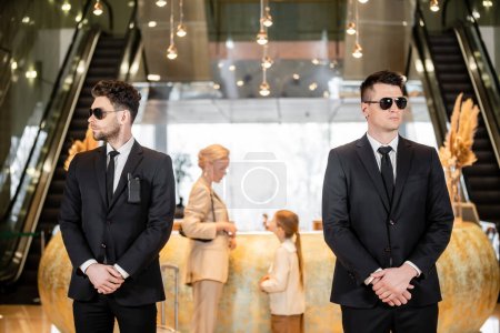 personal security, handsome bodyguards in suits and sunglasses protecting mother and child in hotel lobby, rich and luxury lifestyle, woman and girl standing at reception desk