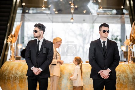 Photo for Personal security, handsome bodyguards in suits and sunglasses protecting mother and child in hotel lobby, luxury lifestyle, woman and girl standing at reception desk - Royalty Free Image