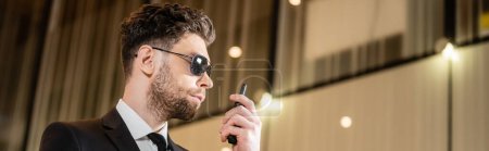 good looking bodyguard, security worker in suit and sunglasses working in lobby of hotel, professional headshots, bearded man using radio transceiver while working in hotel, banner 