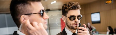 Photo for Bodyguard service, private security, handsome man in sunglasses and formal wear communicating with his working partner by walkie talkie, hotel security, vigilance, professionals, banner - Royalty Free Image