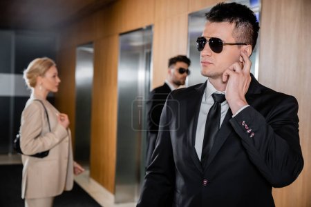 service de garde du corps, protection individuelle, femme blonde en tenue formelle debout près des ascenseurs, personnel de sécurité protégeant femme d'affaires réussie à l'hôtel, bel homme avec oreillette 