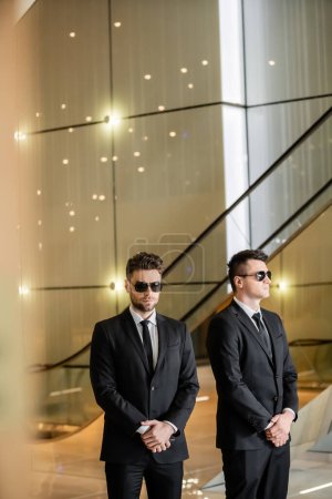 Foto de Gestión de la seguridad del hotel, dos hombres guapos en ropa formal y gafas de sol, guardaespaldas de guardia, medidas de seguridad, vigilancia, trajes y corbatas, seguridad privada, fuertes guardias, vida de lujo - Imagen libre de derechos