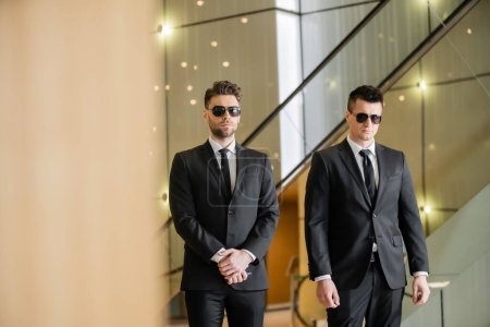 Sicherheitsmaßnahmen eines Luxushotels, zwei gut aussehende Wachen in formeller Kleidung und Sonnenbrille, diensthabende Leibwächter, Sicherheit und Wachsamkeit, schwarze Anzüge und Krawatten, private Sicherheitskräfte, starke Männer