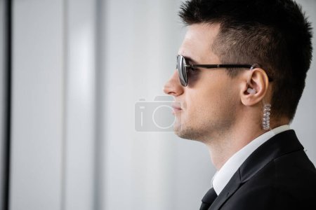 Photo for Professional headshots, bodyguard work, side view of handsome man in sunglasses and black suit with tie, hotel safety, security management, surveillance and vigilance, guard on duty - Royalty Free Image