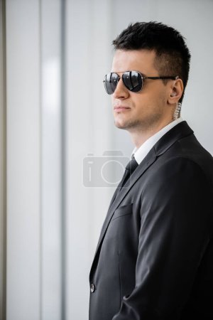 Photo for Professional headshots, bodyguard with earpiece, good looking man in sunglasses and black suit with tie, hotel safety, security management, surveillance and vigilance, uniformed guard on duty - Royalty Free Image