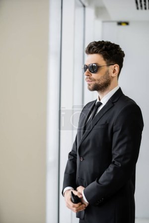 Photo for Surveillance, bodyguard standing with walkie talkie, handsome security man in sunglasses and black suit with tie, hotel safety management, uniformed guard on duty, professional headshots - Royalty Free Image
