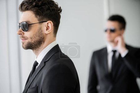 Photo for Surveillance, bodyguard in sunglasses and black suit with tie, hotel safety, security management, uniformed guard on duty, work partner on blurred background, personal protection - Royalty Free Image