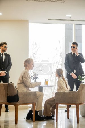 security service, private safety concept, bodyguards standing near female clients, preteen girl and blonde mother spending time together in cafe, personal safety and protection 
