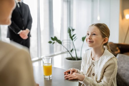 happy preteen girl talking to mother near bodyguard on blurred background, security service, private safety concept, glass of orange juice, personal safety, rich lifestyle, 