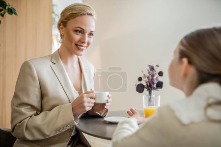 mother and daughter spending quality time together, happy blonde woman talking to preteen girl and holding cup of coffee, working parent and kid, modern parenting, family bonding, brunch 