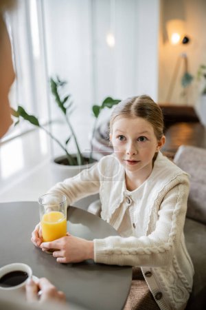 Photo for Mother and daughter spending quality time together, preteen girl holding glass of orange juice and looking at mother, working parent and kid, modern parenting, family bonding, blurred foreground - Royalty Free Image
