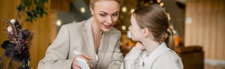 Photo for Happy mother and daughter spending quality time together, blonde woman holding smartphone near daughter, digital age, working parent and kid, modern parenting, family bonding, banner - Royalty Free Image