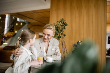 Photo for Mother and daughter spending quality time together, blonde woman smiling and hugging preteen girl, orange juice and cup of coffee, working parent and kid, modern parenting, family bonding - Royalty Free Image